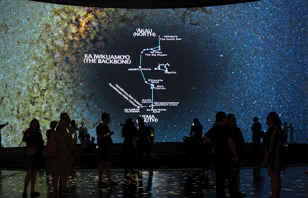 silhouette of people watching a screen projection of the ocean with a route